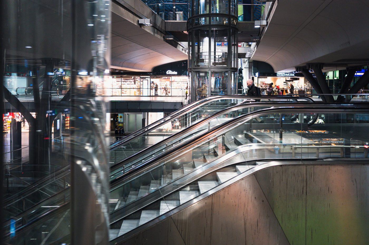 Glass escalators leading toward the lit shop windows of a station, Berlin