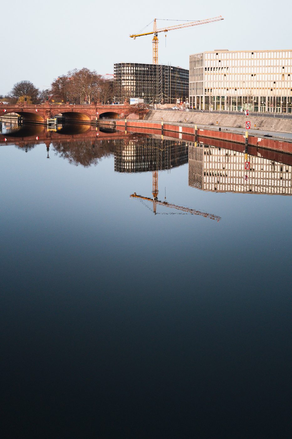 Red brick bridge and construction crane reflected in the Spree, Berlin