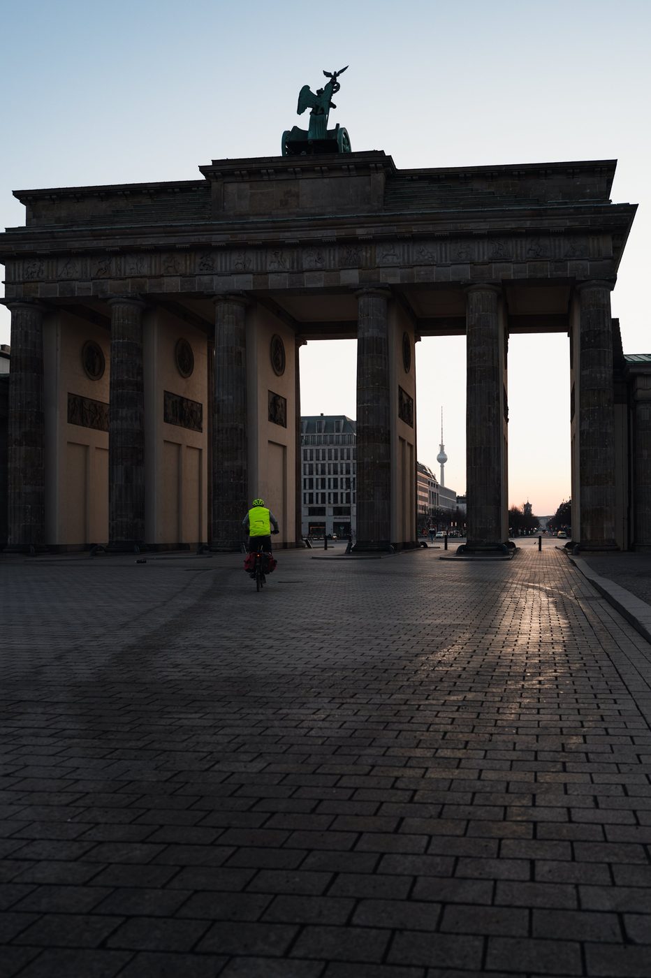 Cyclist in a fluorescent jacket crossing through the Brandenburg Gate at dawn, Berlin