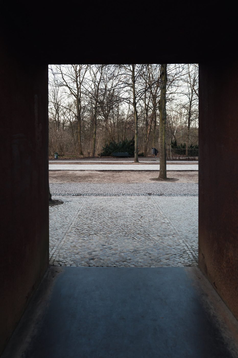 Rusted metal frame opening onto a paved, tree-lined path, Berlin