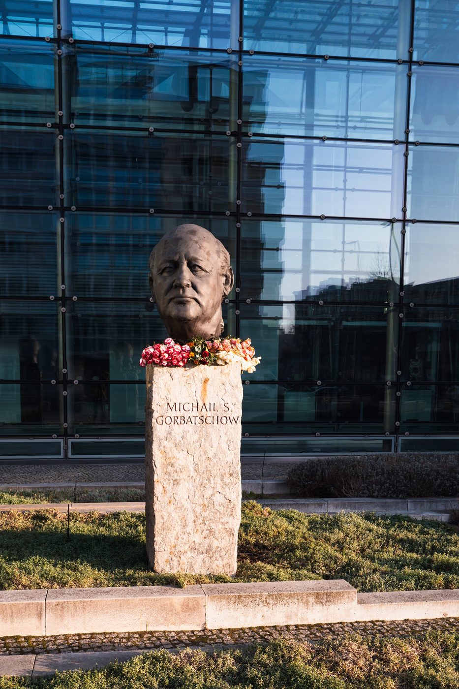 Flower-adorned bronze bust of a former leader in front of a glass facade, Berlin