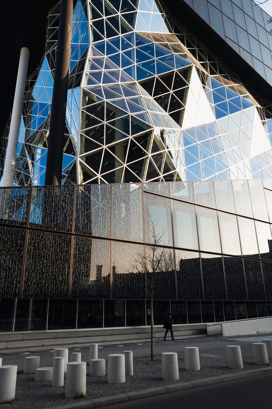 Glass facade with angular geometric shapes and a passerby, Berlin