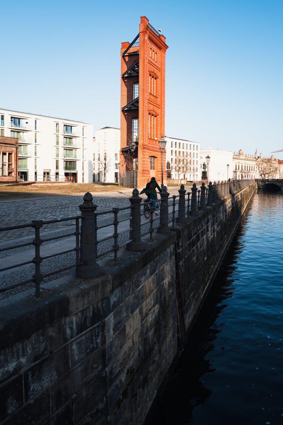 Red brick tower beside a canal, a cyclist riding along the quay, Berlin