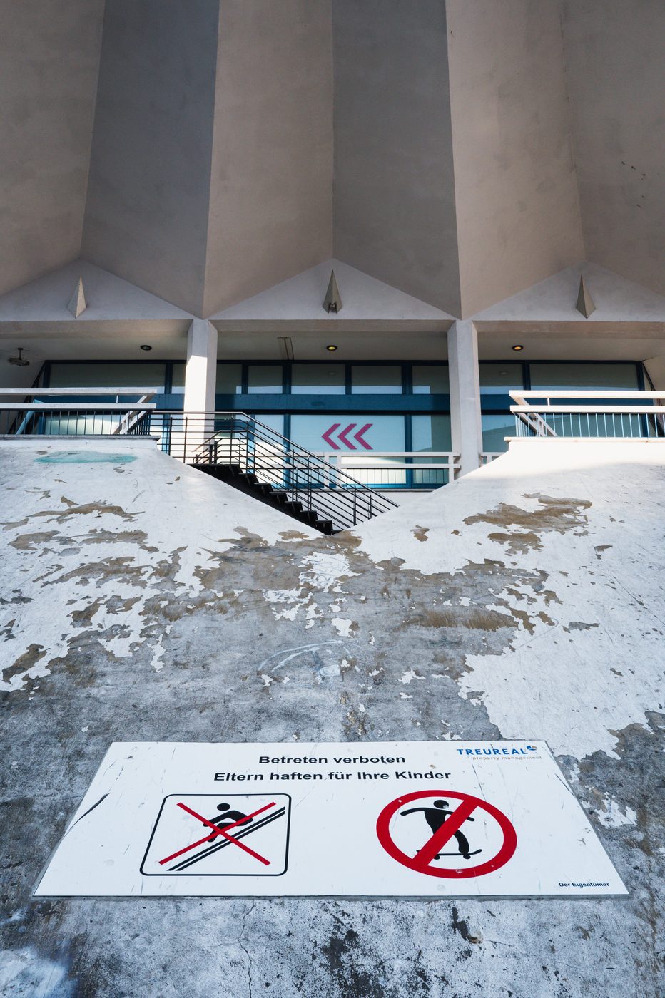 Eroded concrete stairs beneath brutalist architecture, prohibition sign, Berlin