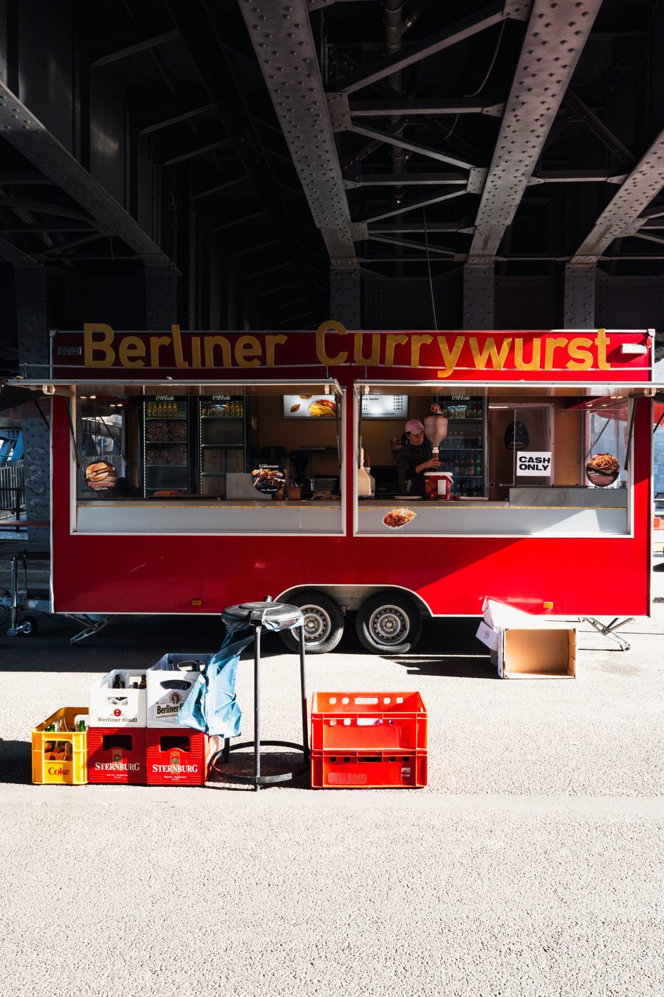 Bright red currywurst truck parked beneath a railway bridge, Berlin
