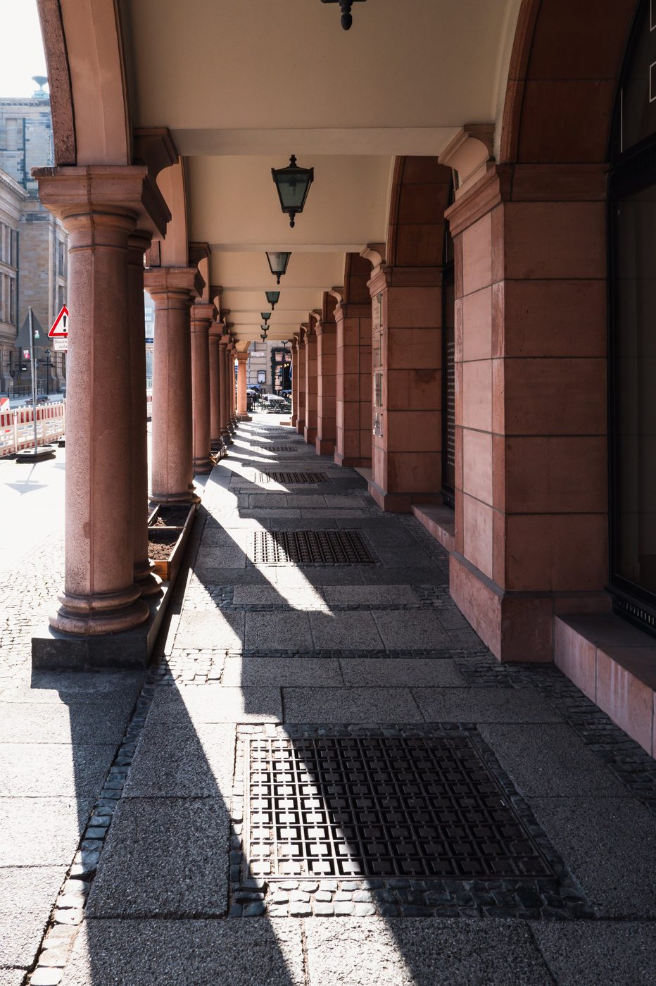 Red sandstone colonnade and hanging lanterns along a sidewalk, Berlin