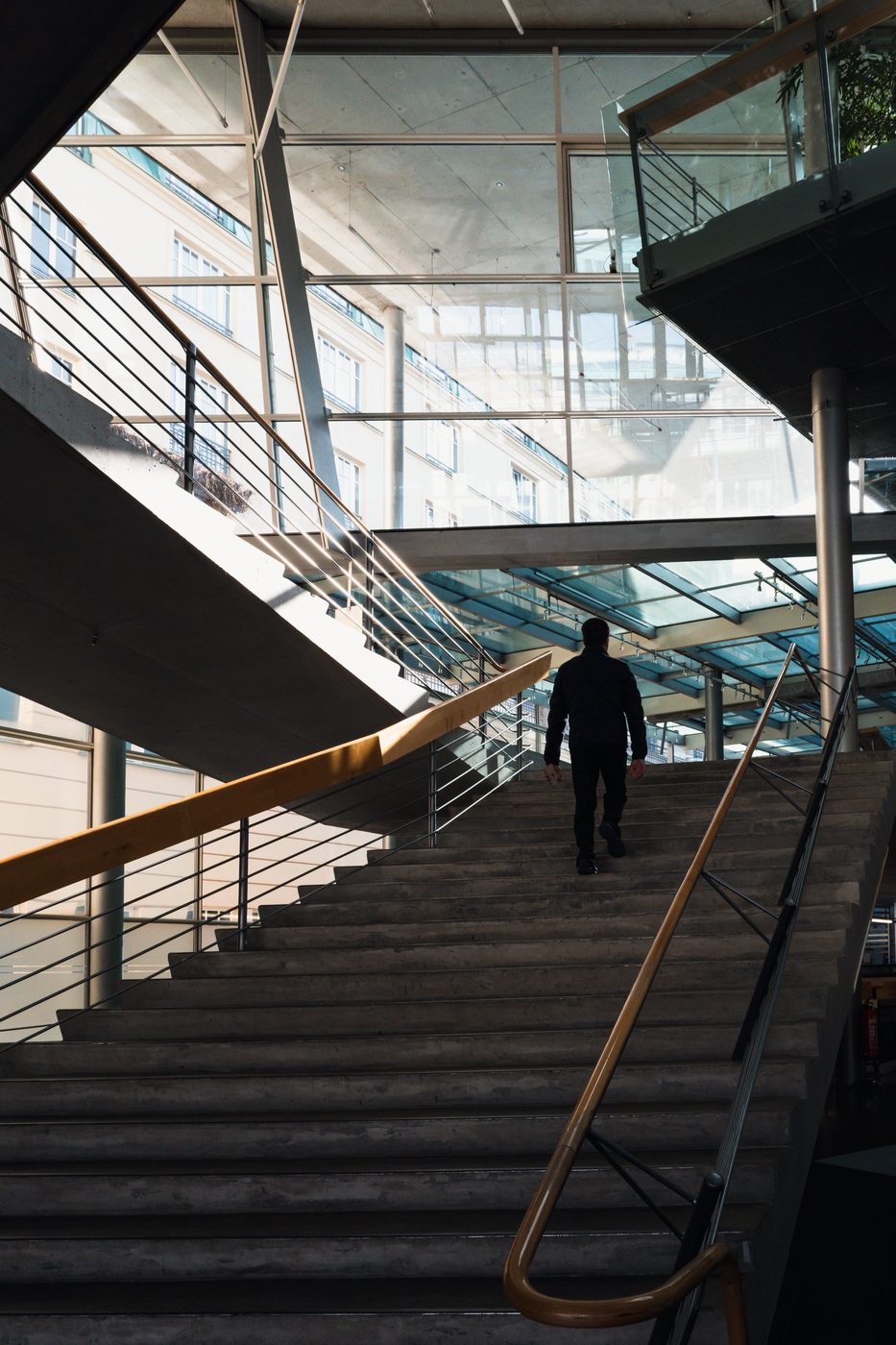 Man climbing a concrete staircase beneath an architectural glass roof, Berlin