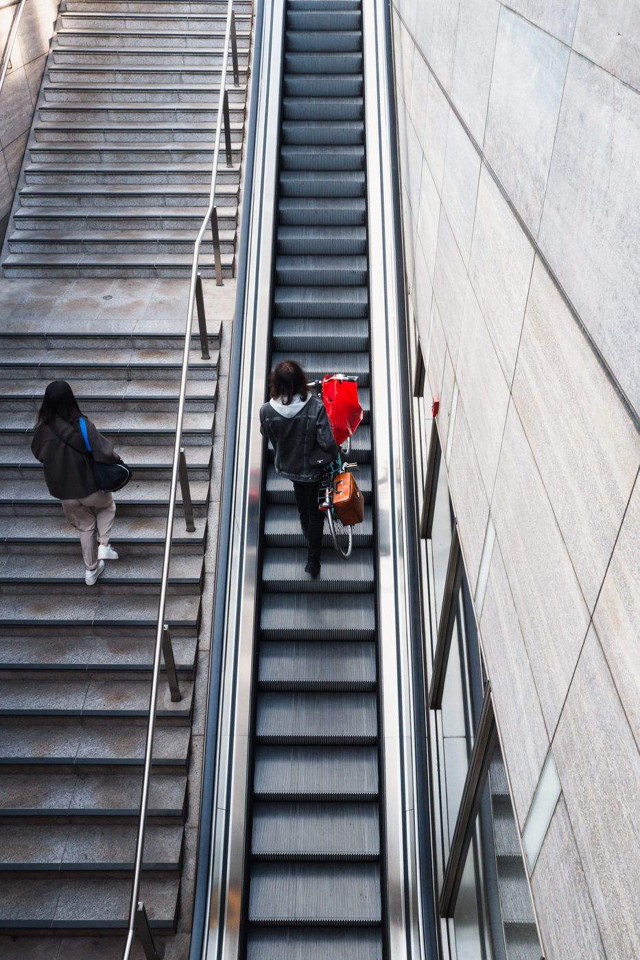 High-angle view of an escalator, a woman pushing a bicycle with a red pannier, Berlin