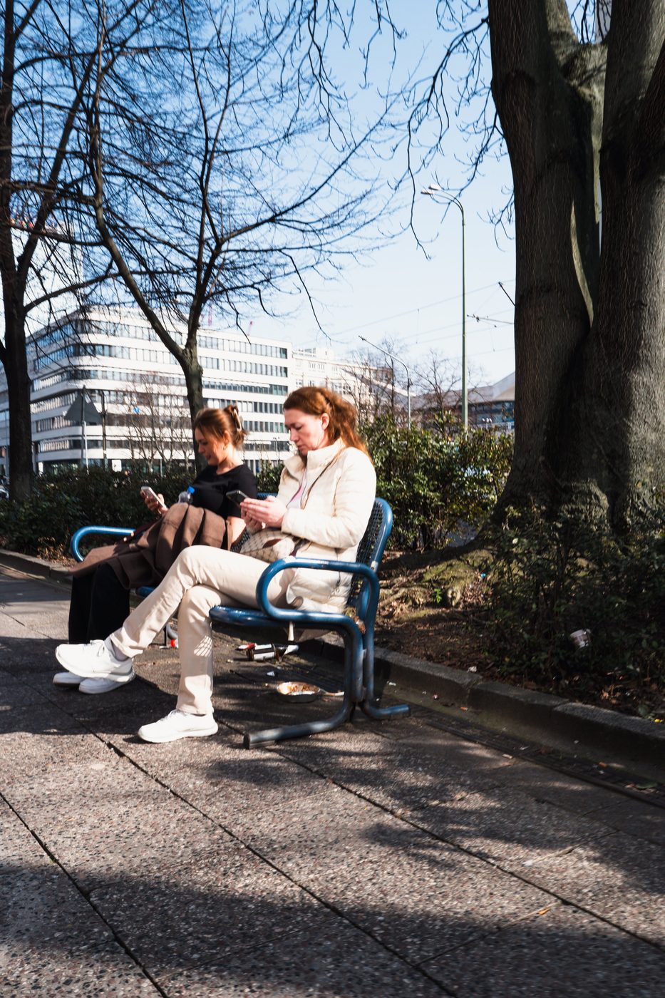 Two women sitting on a bench, absorbed in their phones, Berlin