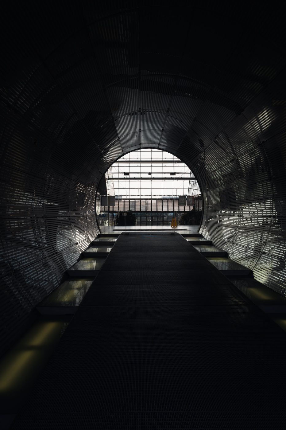 Ribbed metal tunnel leading toward a bright glass exit, Berlin
