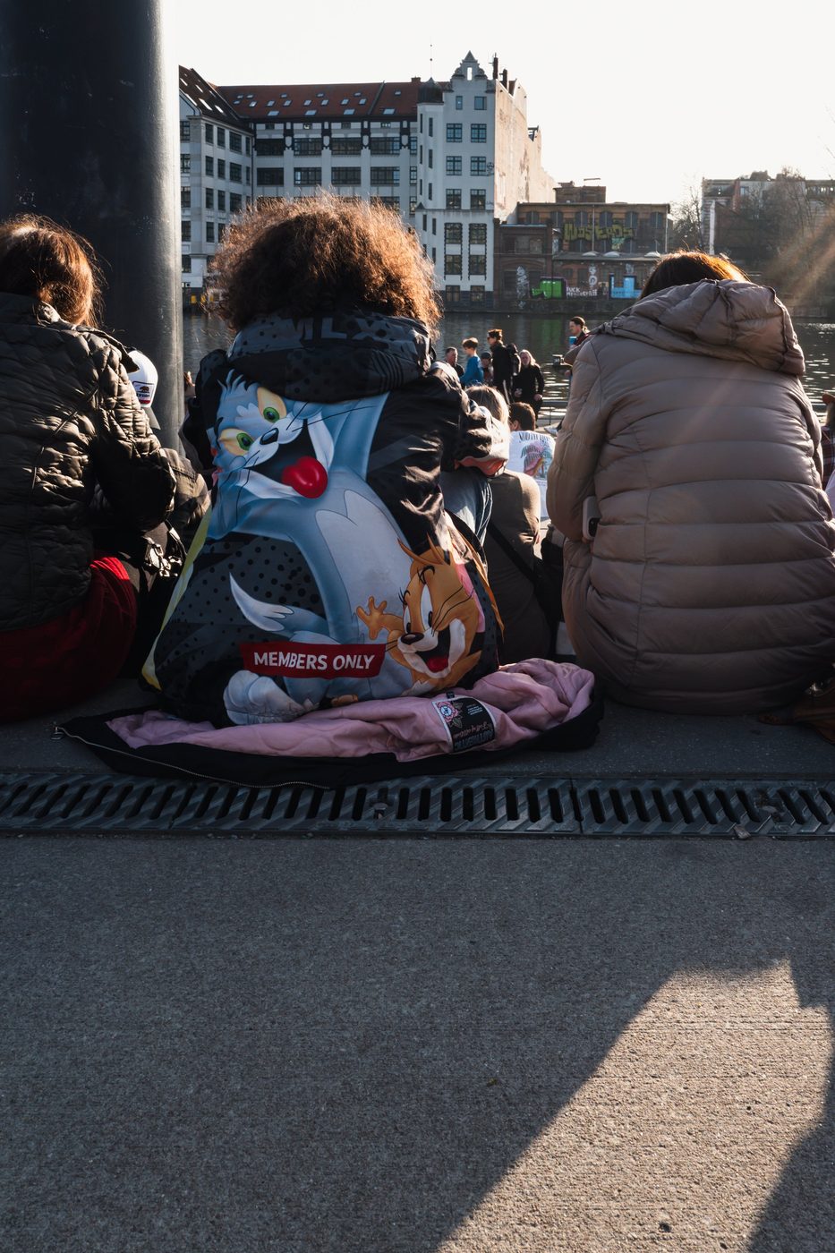 Back of a jacket with a cartoon print among passersby sitting by the Spree, Berlin
