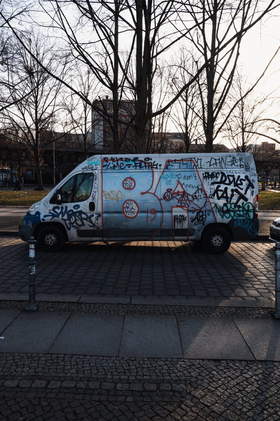 White van entirely covered in graffiti, parked beneath the trees, Berlin