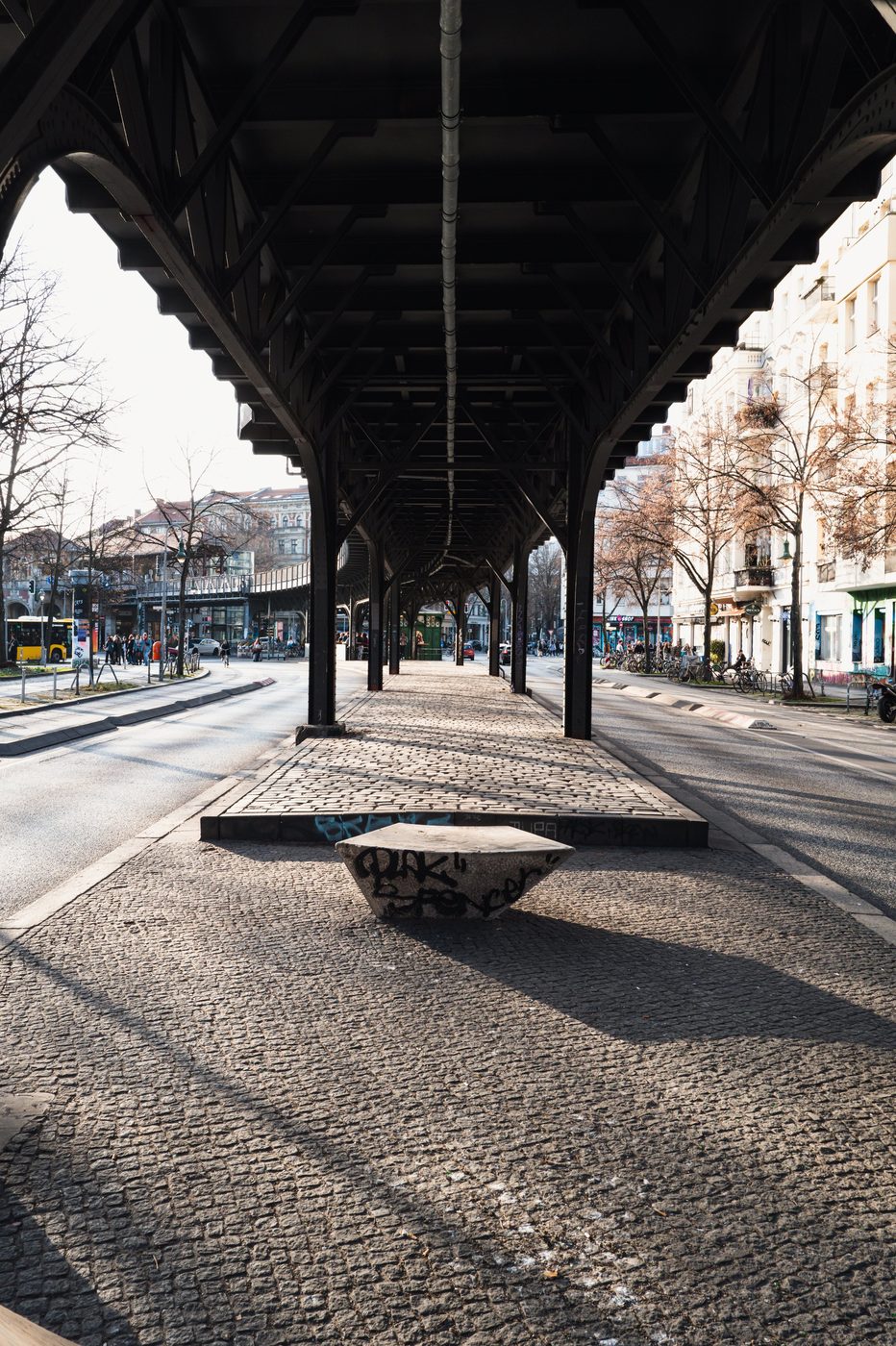 Metal railway viaduct looming over a tagged concrete bench, Berlin