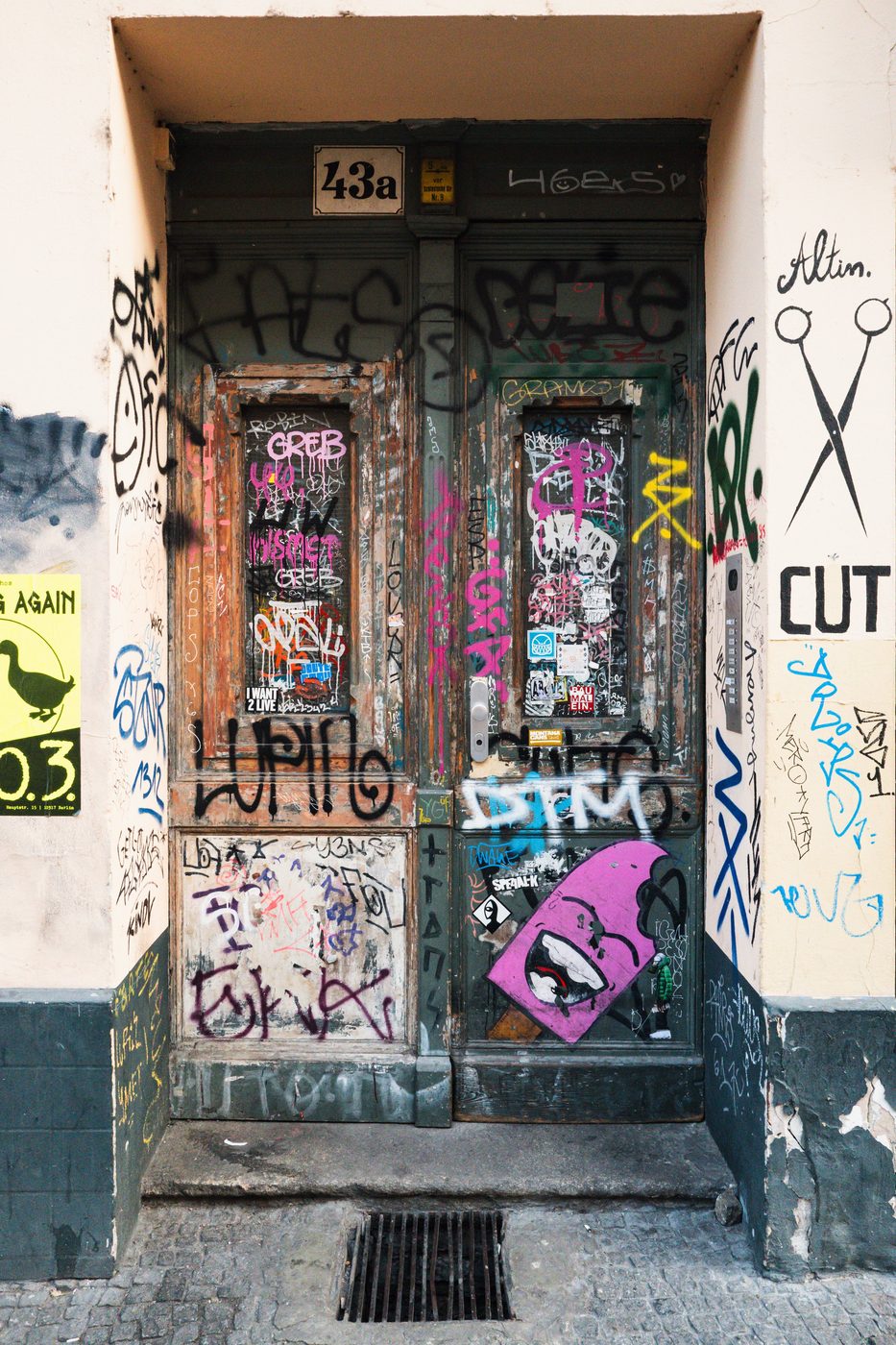Wooden door striped with graffiti, scissors painted on the neighboring wall, Berlin