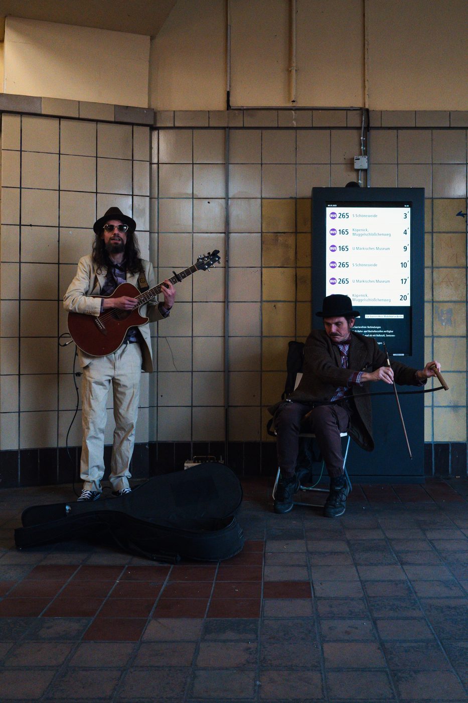 Pair of street musicians playing guitar and musical saw in a tiled corridor, Berlin