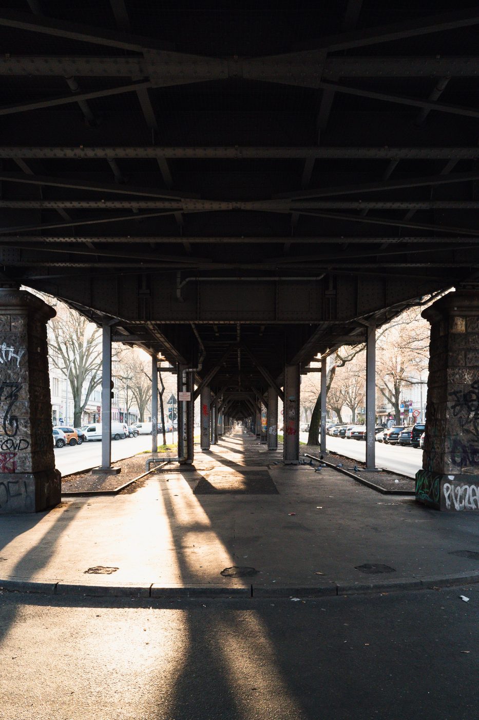 Symmetry of a shadowed railway viaduct above a street lined with cars, Berlin