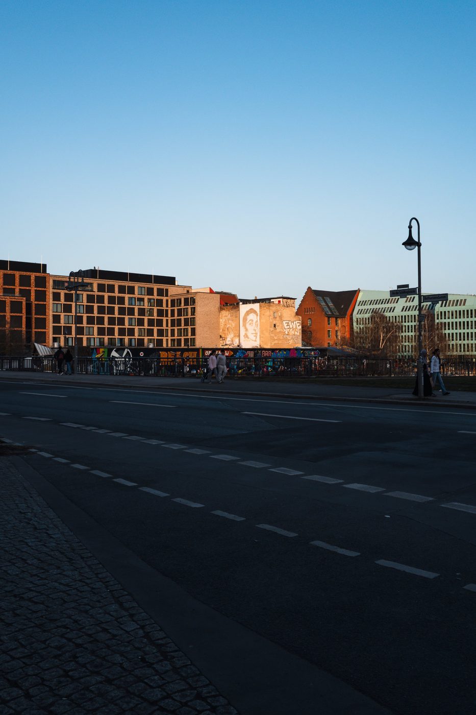Wall lit by raking light and adorned with a painted portrait, seen from afar, Berlin