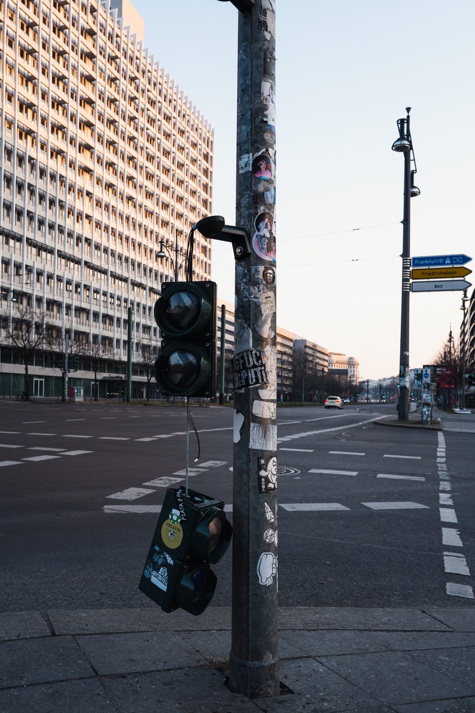 Traffic light riddled with stickers facing a brutalist building, Berlin