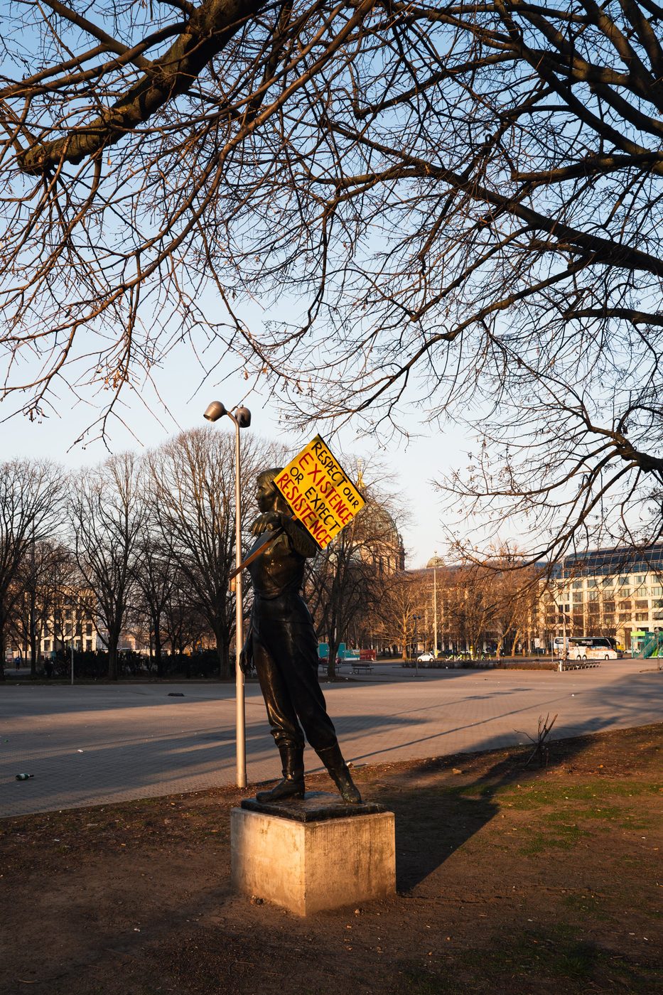 Statue of a woman holding up a protest sign beneath a bare tree, Berlin