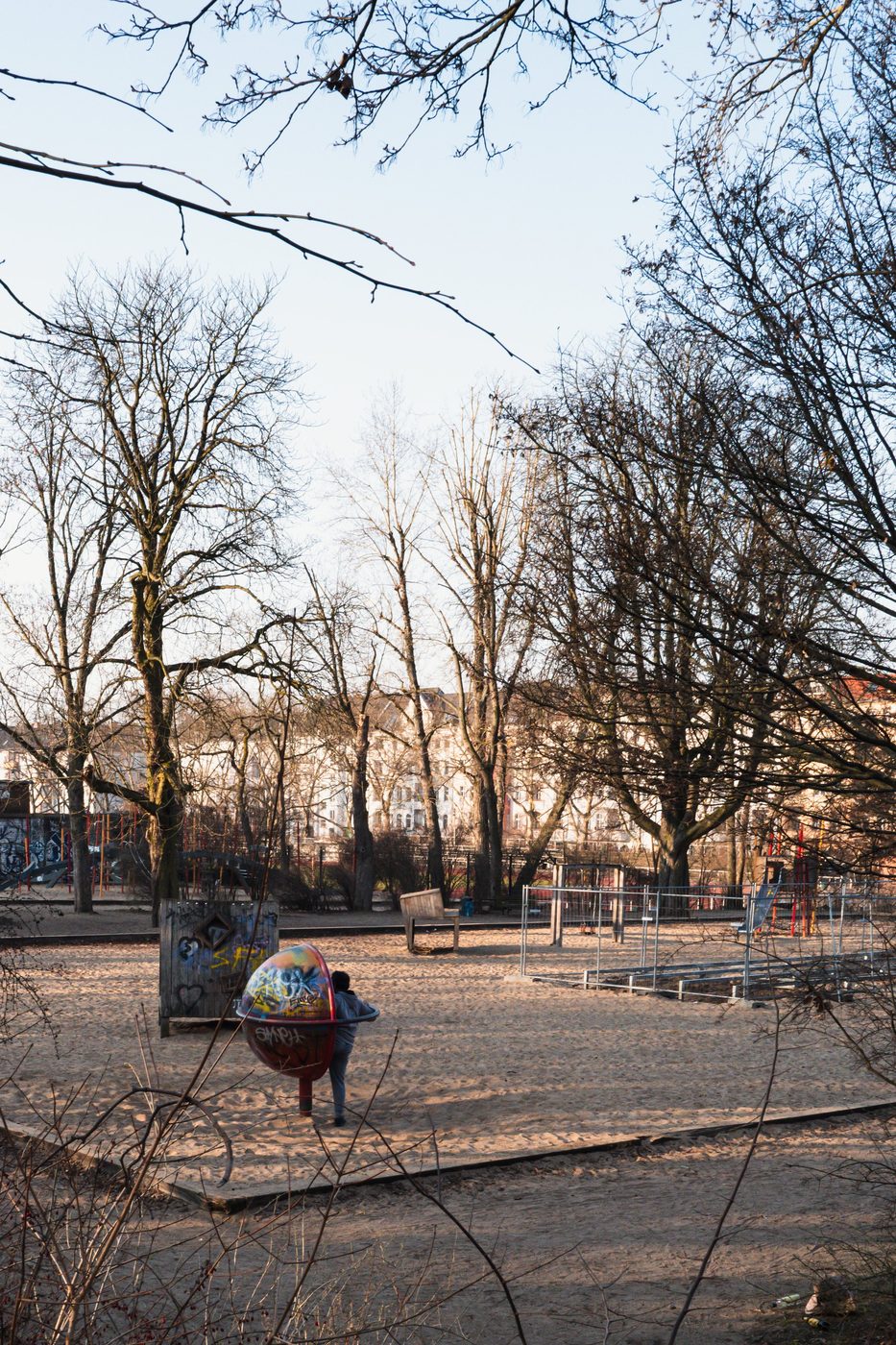 Child playing on a round, graffiti-covered structure in a playground, Berlin