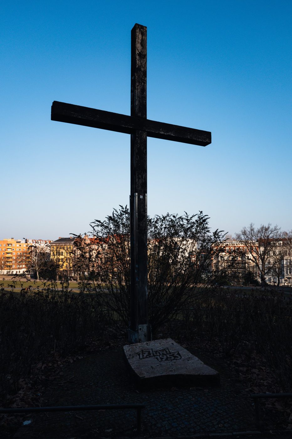 Wooden memorial cross planted amid a bed of shrubs, Berlin