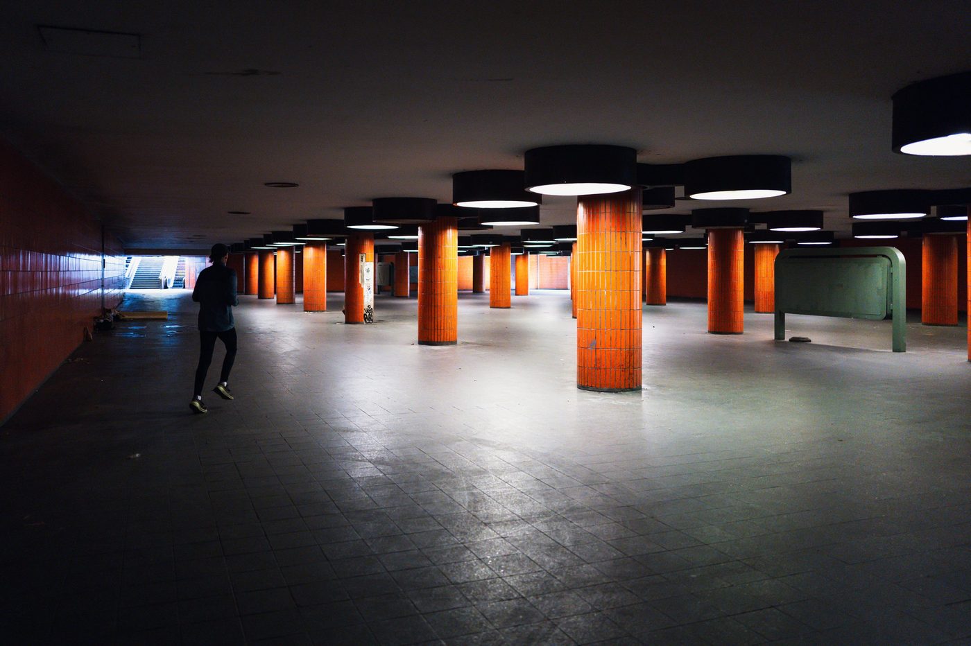 Lone runner crossing an underground hall with orange columns, Berlin