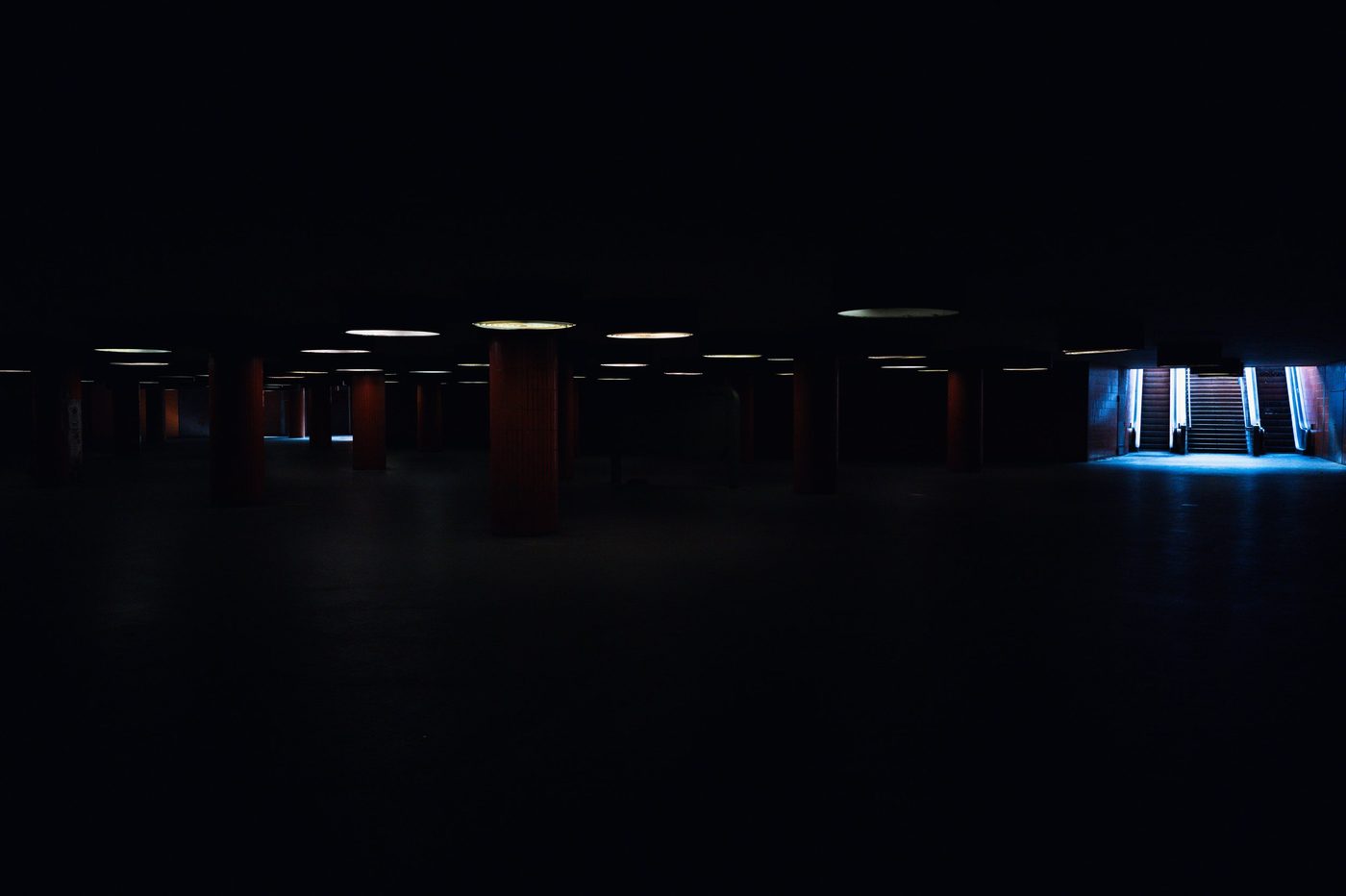 Columns plunged into darkness facing a lit escalator in the distance, Berlin