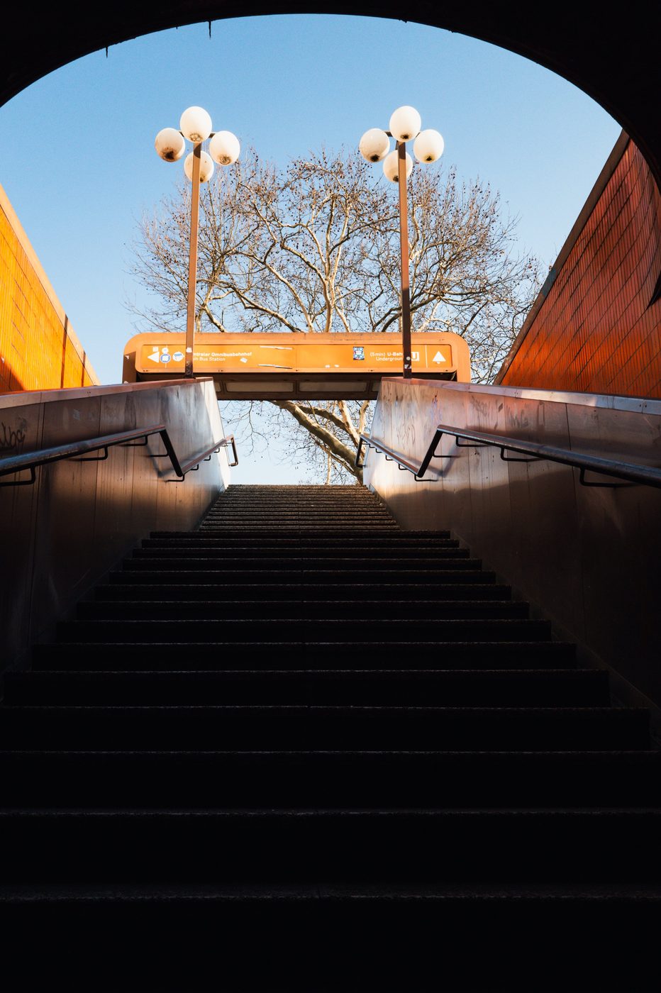 View from an underground staircase toward a tree and round streetlamps, Berlin