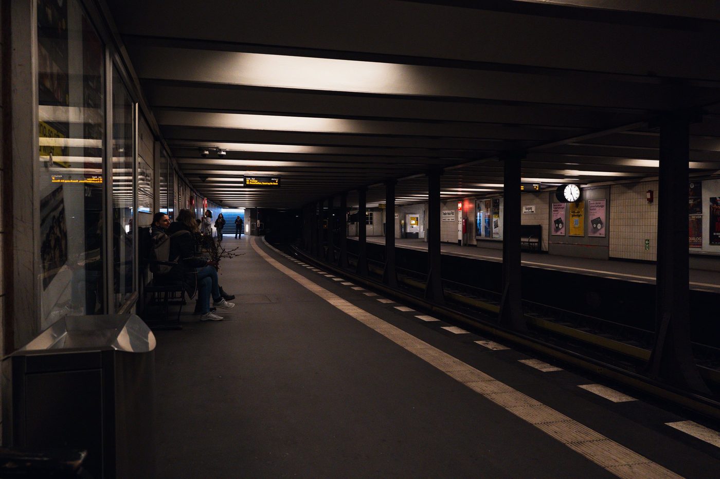 Tiled subway platform where passengers wait beneath a clock, Berlin