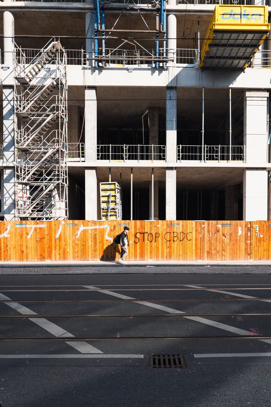 Passerby walking past a construction fence tagged with a protest message, Berlin