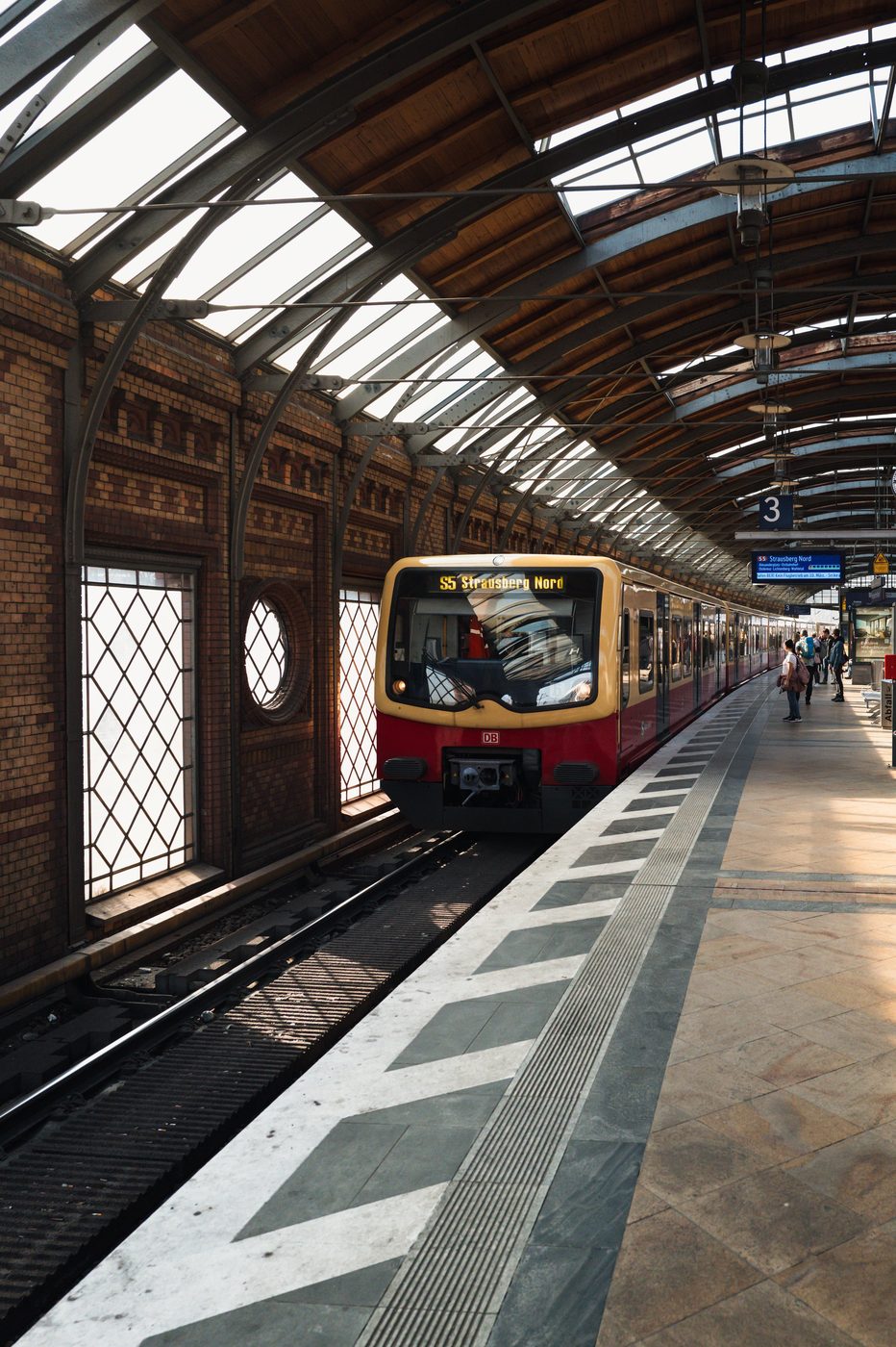 Red and yellow regional train entering beneath a station's ornate glass roof, Berlin