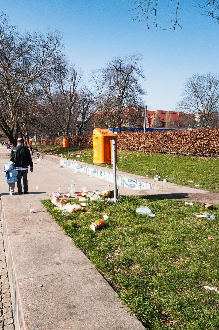 Father and child walking along a lawn littered with debris, Berlin