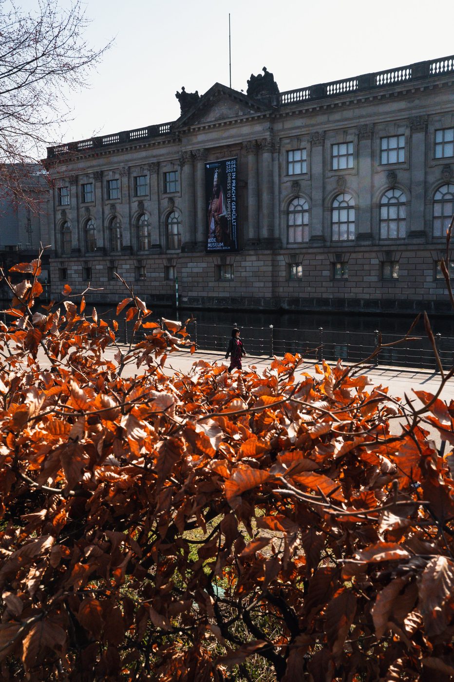 Woman walking past the Bode Museum, russet foliage in the foreground, Berlin