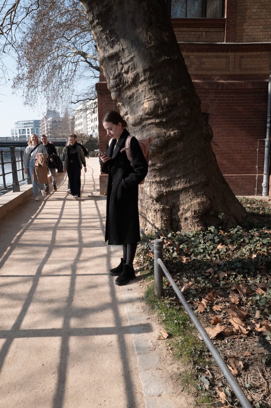 Woman leaning against a century-old tree, cast shadows of a railing, Berlin