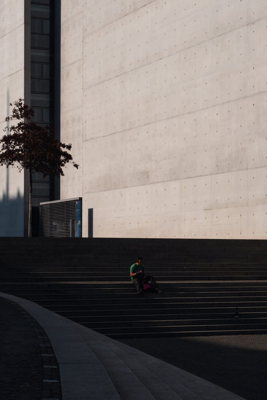Man sitting alone on wide steps facing a concrete wall, Berlin