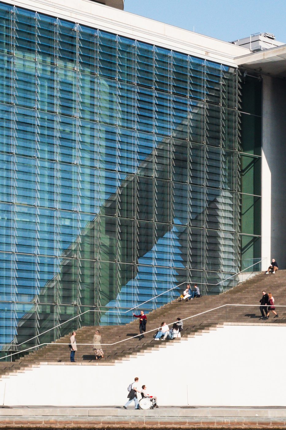 Diagonal reflections on a glass facade, passersby sitting on a staircase, Berlin
