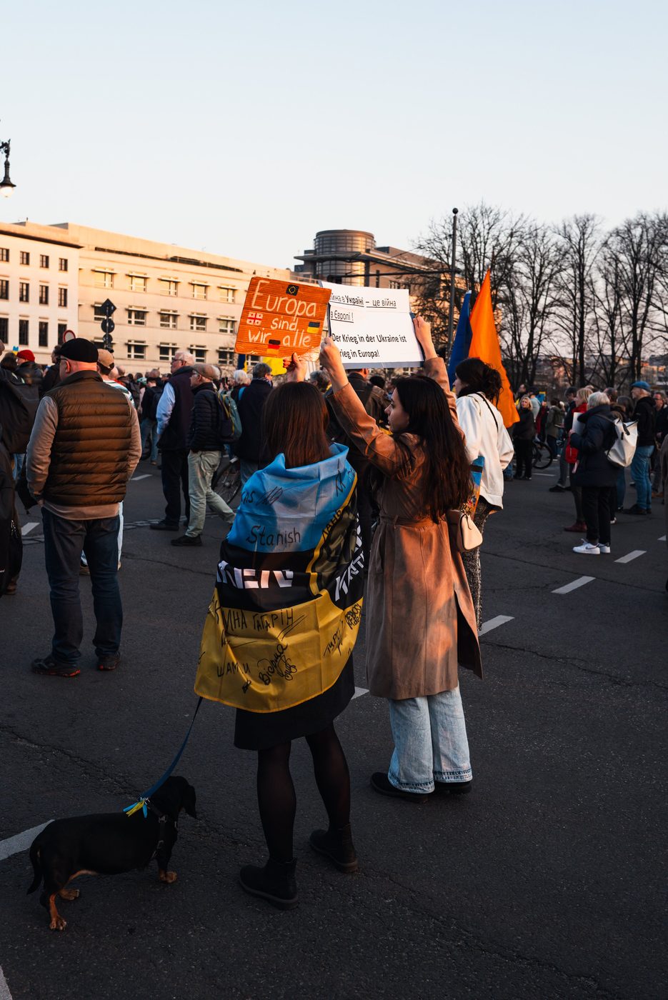 Female protesters holding solidarity signs, a leashed dog in the foreground, Berlin