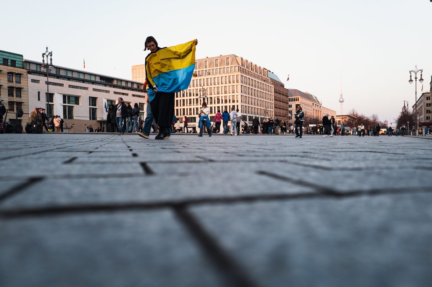 Woman wearing a Ukrainian flag over her shoulders, television tower in the distance, Berlin