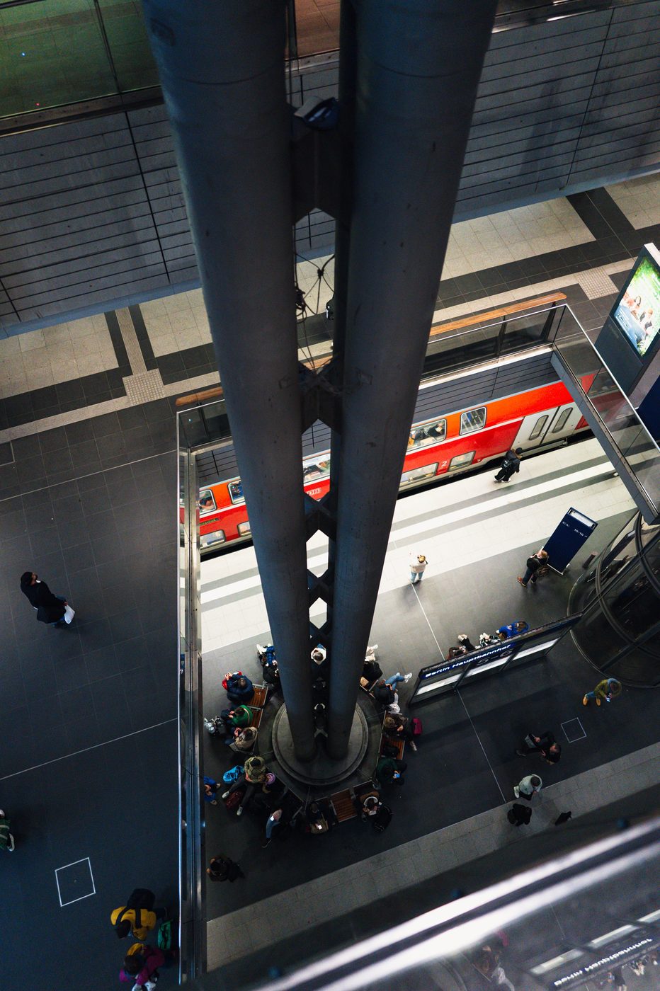 High-angle view between two massive pillars overlooking a platform and its red train, Berlin
