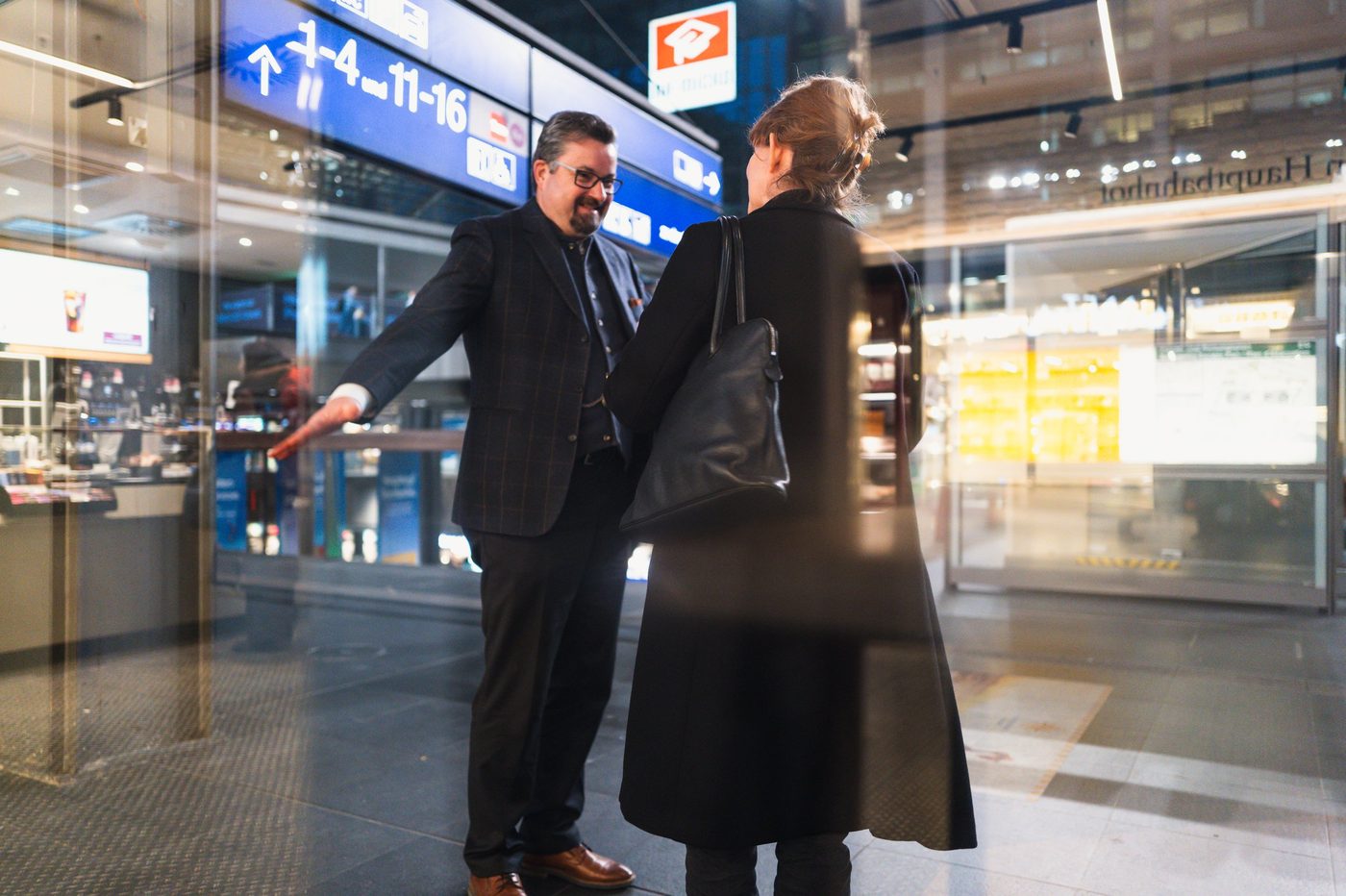 Couple talking through a window reflecting the signs of the central station, Berlin