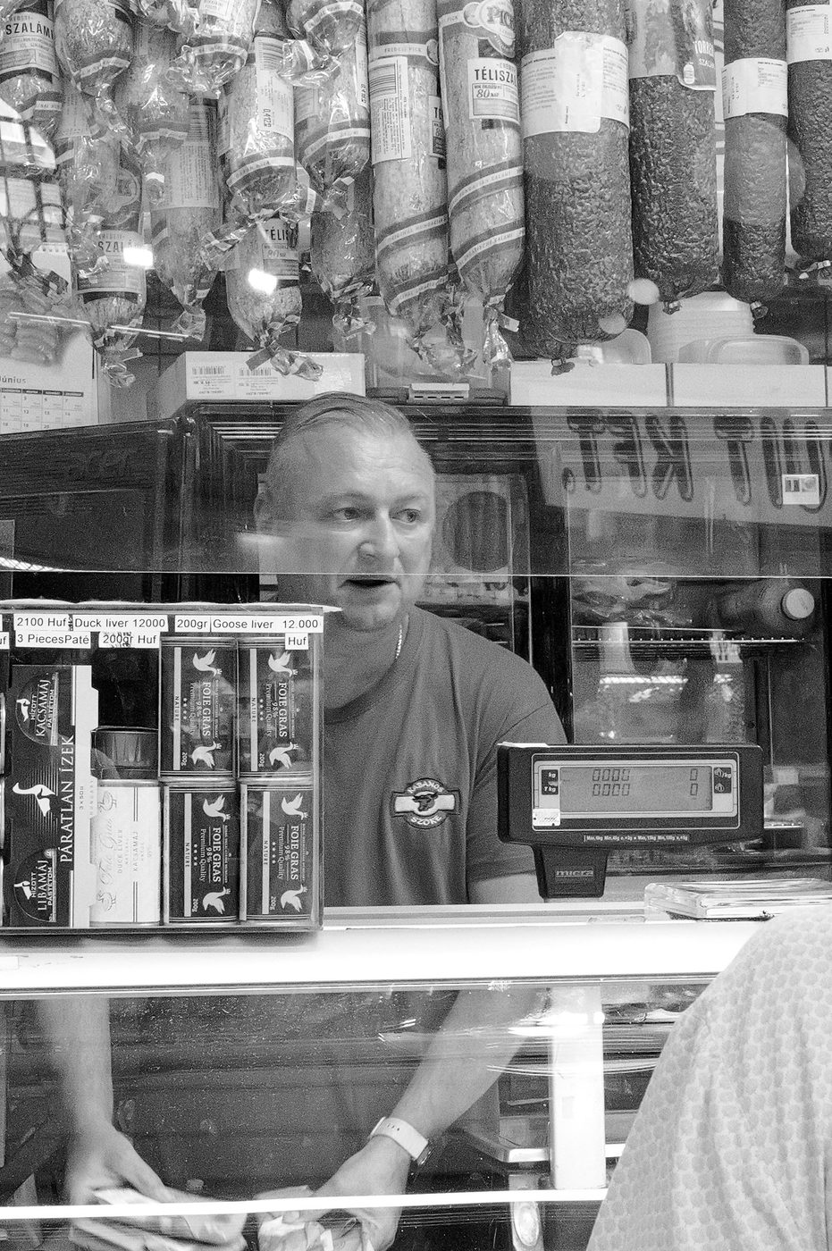 A butcher serving a customer under hanging sausages, Budapest