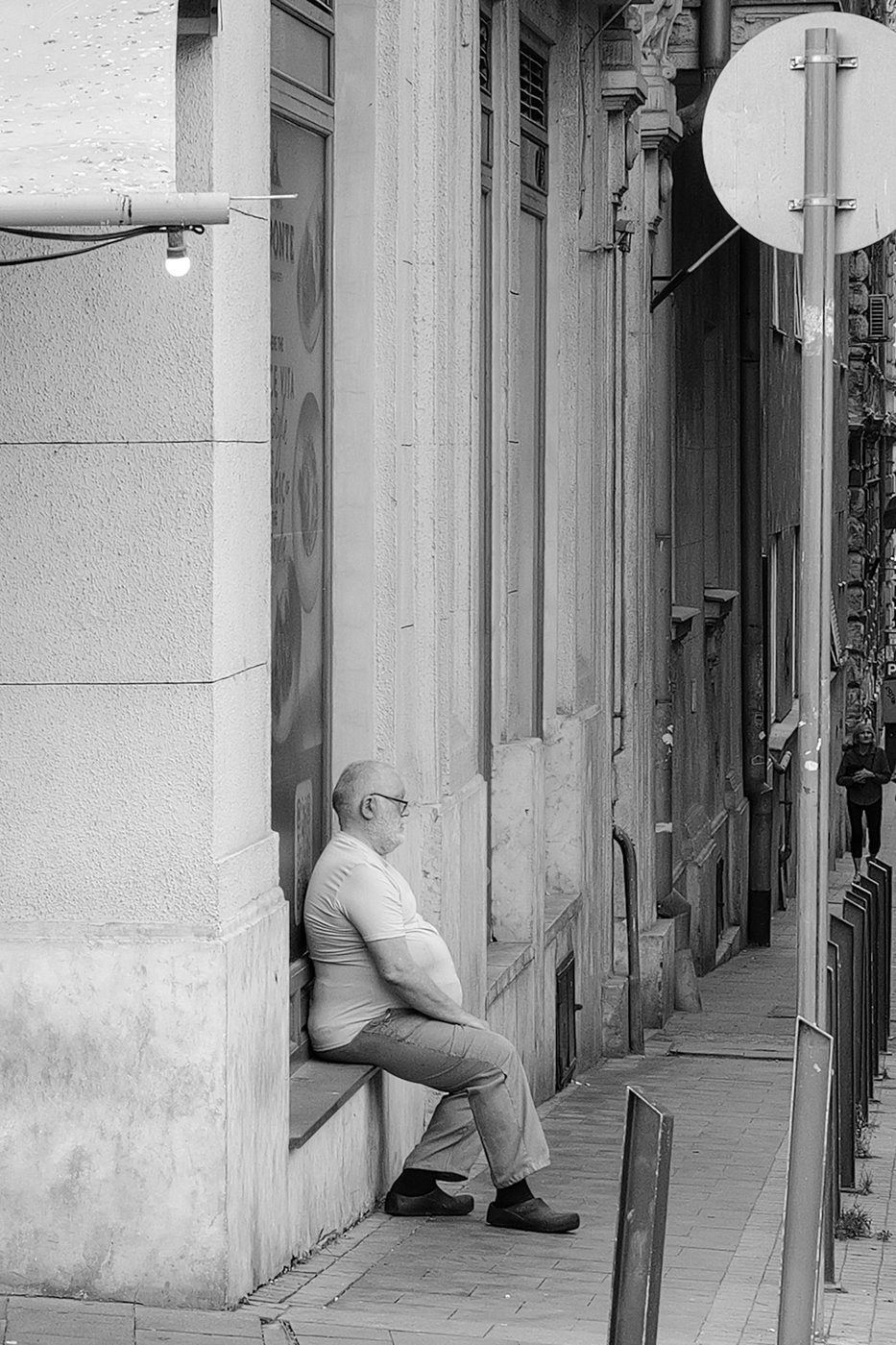 A man sitting in profile, resting in a shop doorway, Budapest
