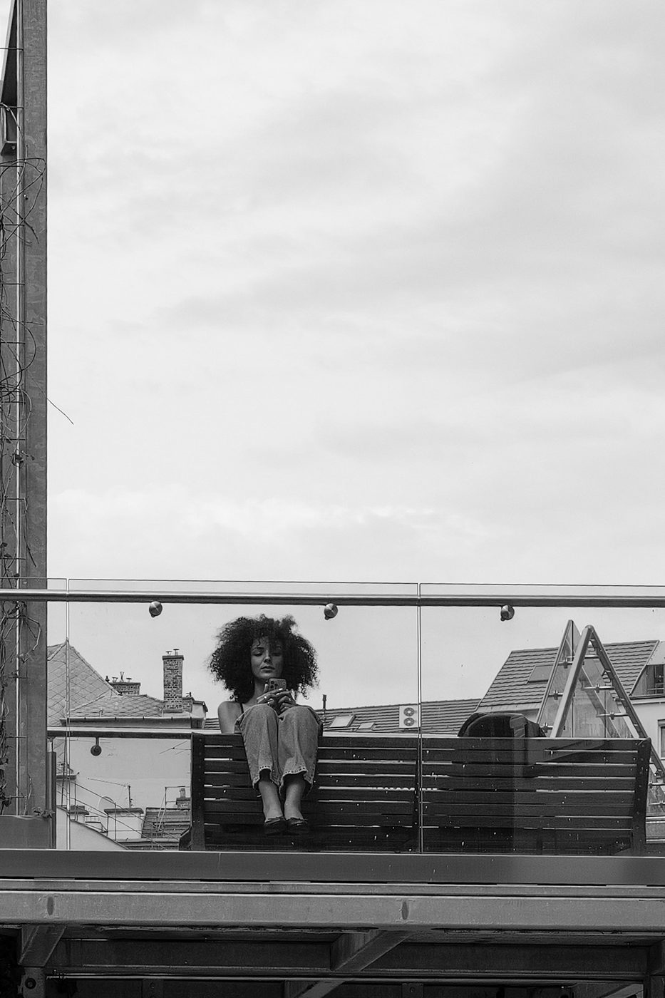 A woman with curly hair sitting on a rooftop terrace bench, Budapest