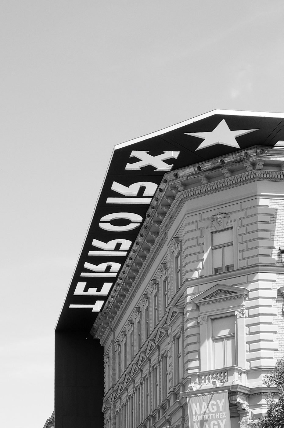 Black triangular sign adorned with a star atop a classical building, Budapest