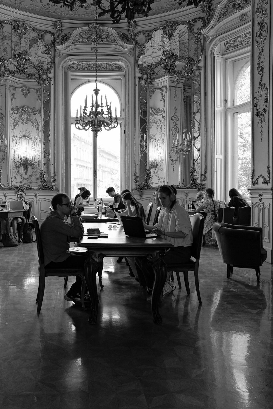 Students seated at a table under a crystal chandelier, baroque hall, Budapest