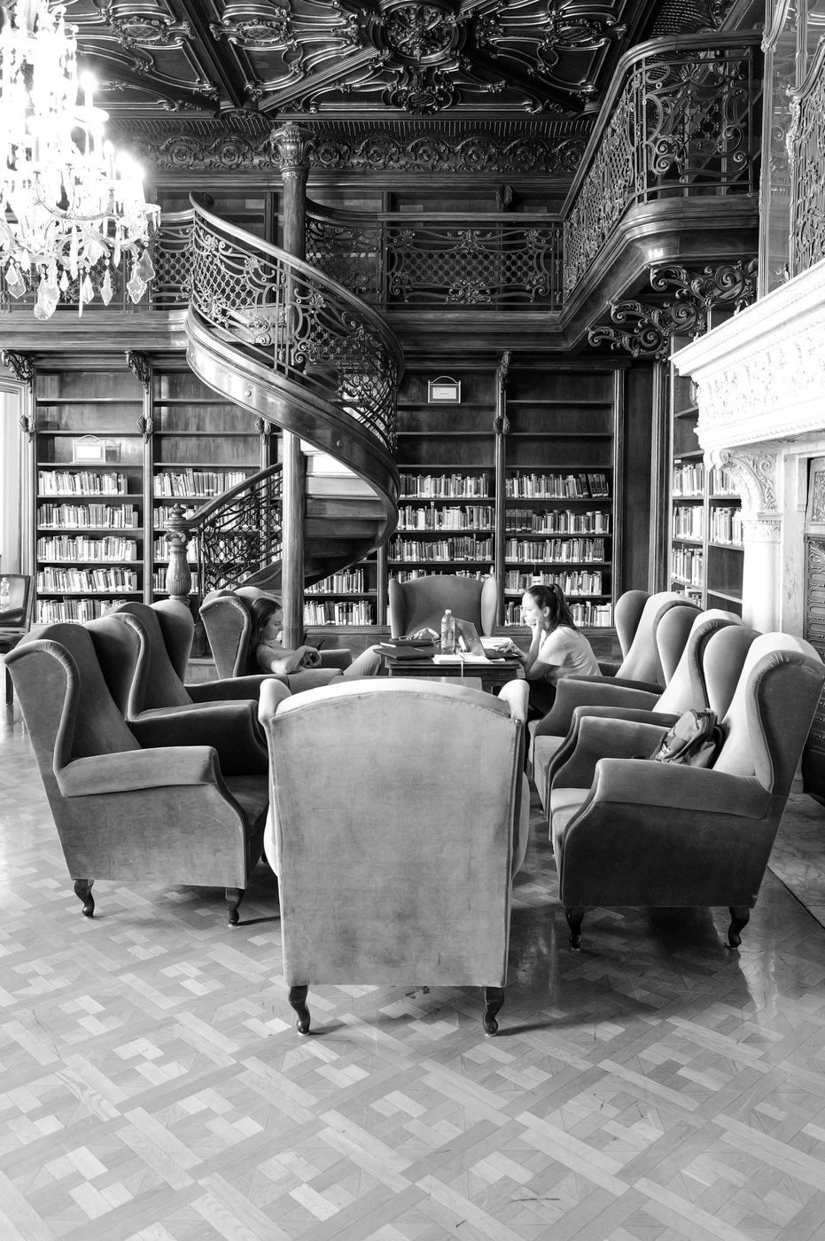 Students around a table near a staircase with a wrought-iron balustrade, Budapest
