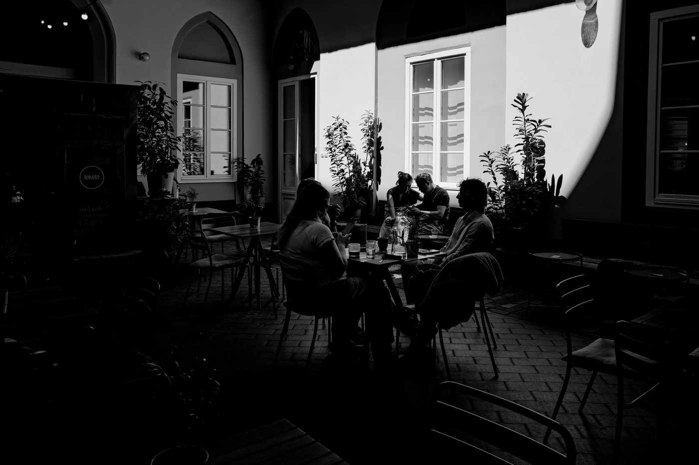 Group seated at a shaded terrace, play of light on a white wall, Budapest