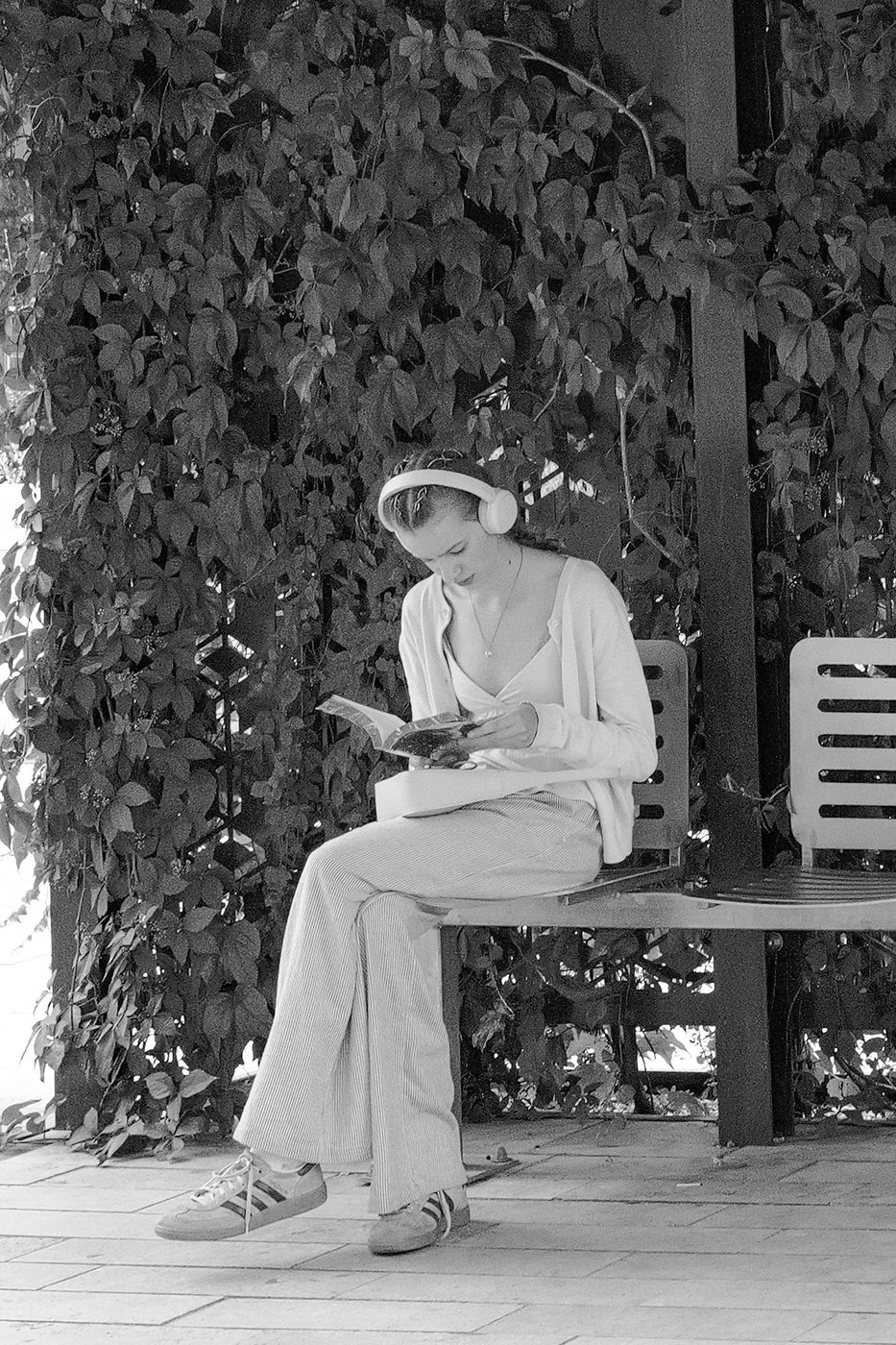 A woman reading with headphones on, sitting under a leafy arbor, Budapest