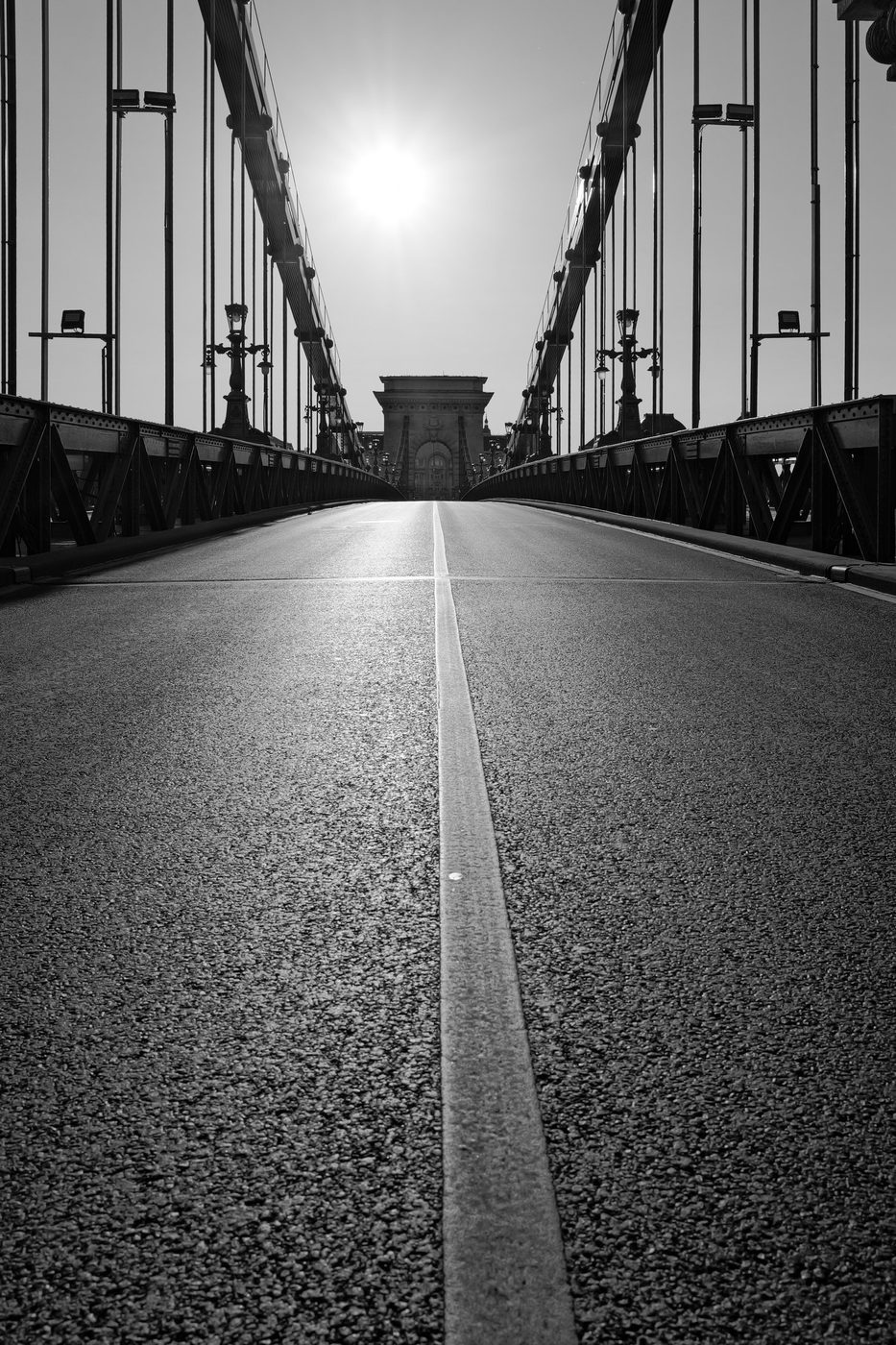 Central white line leading toward the arch of a suspension bridge, Budapest