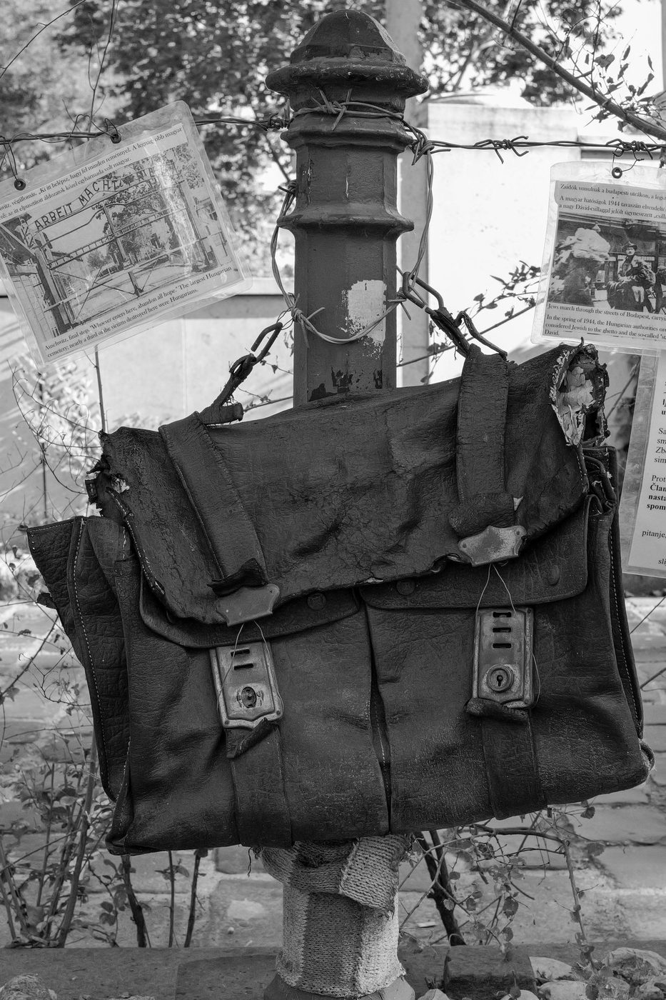 Worn leather bag and historical documents attached to a memorial post, Budapest
